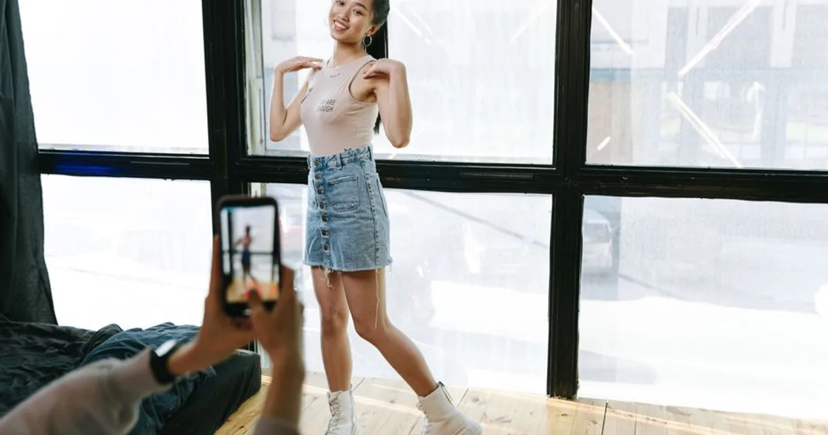 A young woman dancing while being recorded on a smartphone in a sunlit modern studio.